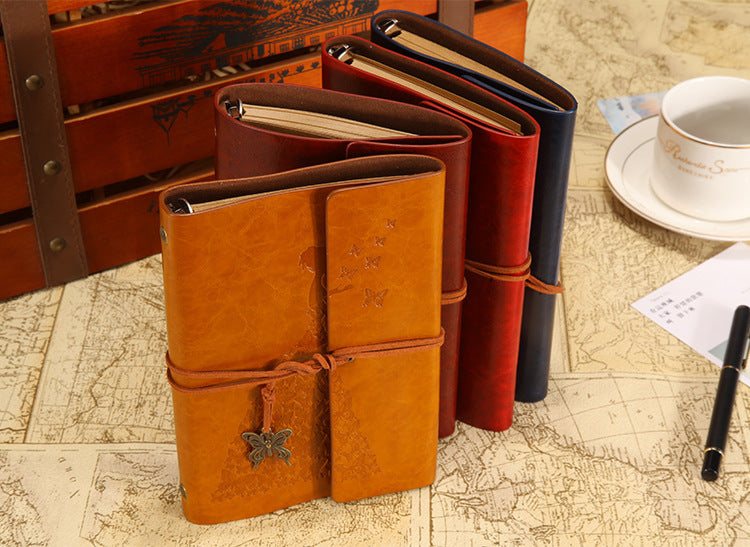A set of vintage butterfly PU leather A6 journal notebooks in various shades of brown and red stacked on a map background.