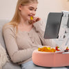 A young woman is using an adjustable pillow tablet and Kindle stand with a soft plush fabric on a pink base.