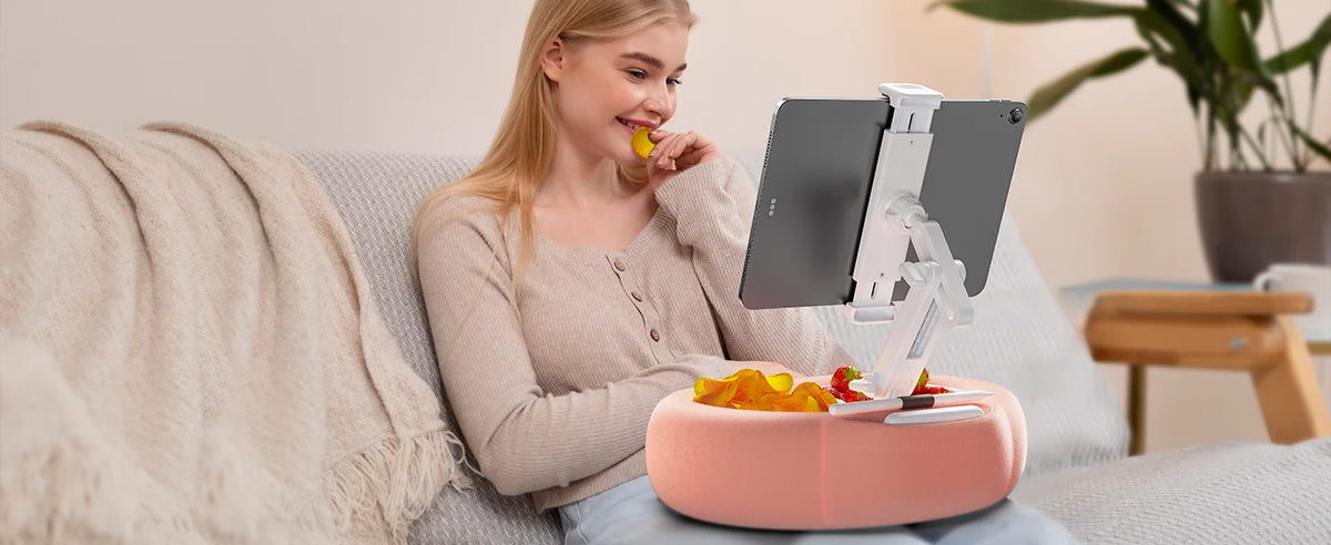A young woman is using an adjustable pillow tablet and Kindle stand with a soft plush fabric on a pink base.