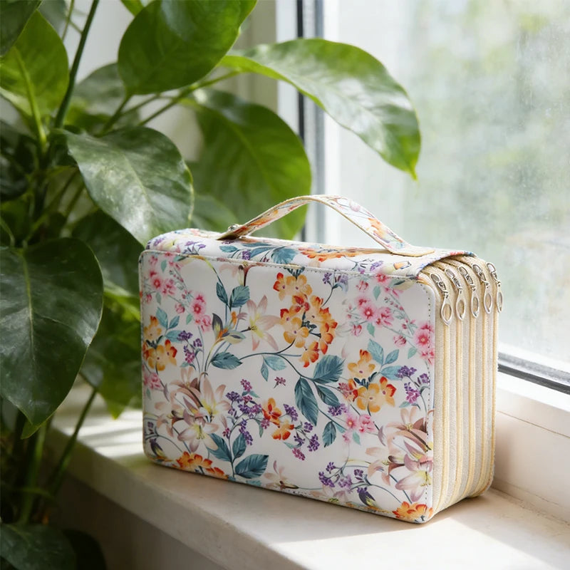 A rectangular pencil case with a floral pattern and striped accents is displayed next to a window with green foliage.