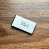 A silver engraved money clip wallet with the name Maik resting on a wooden surface.