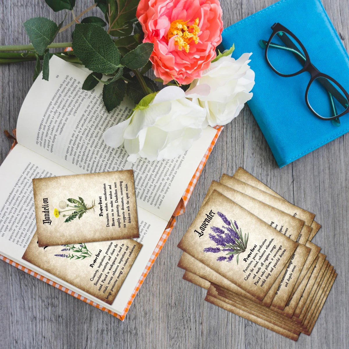 A stack of botanical herbal reference cards with pressed flowers and text resting on an open journal and a blue notebook.