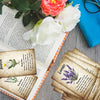 A collection of botanical herbal reference cards featuring pressed flowers and text, laid out on a wooden surface.