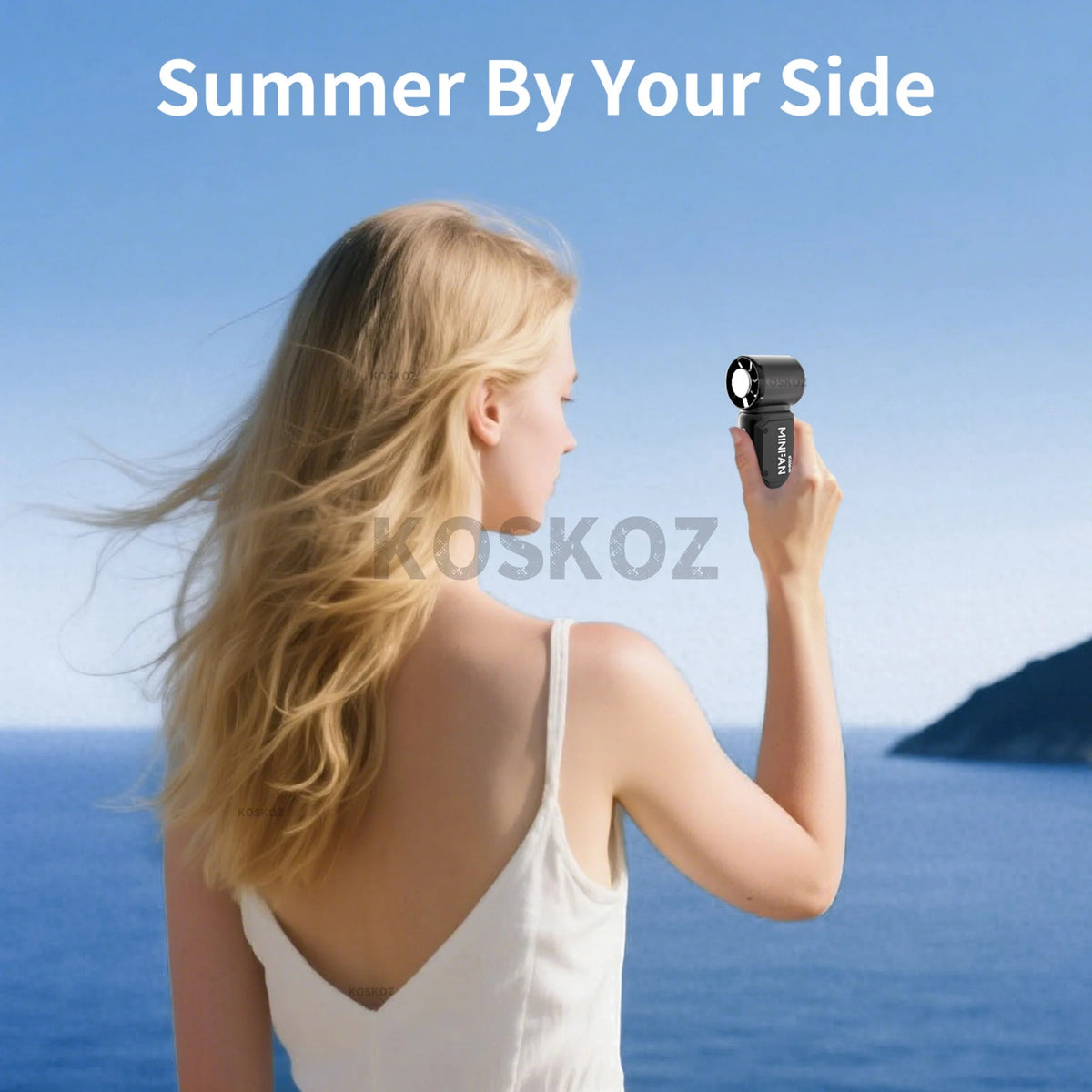 A blonde woman holds a black mini portable ice cooling fan against the blue sea background.