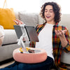 A young man is smiling while holding an adjustable pillow tablet and Kindle stand with a soft plush fabric on a sofa.