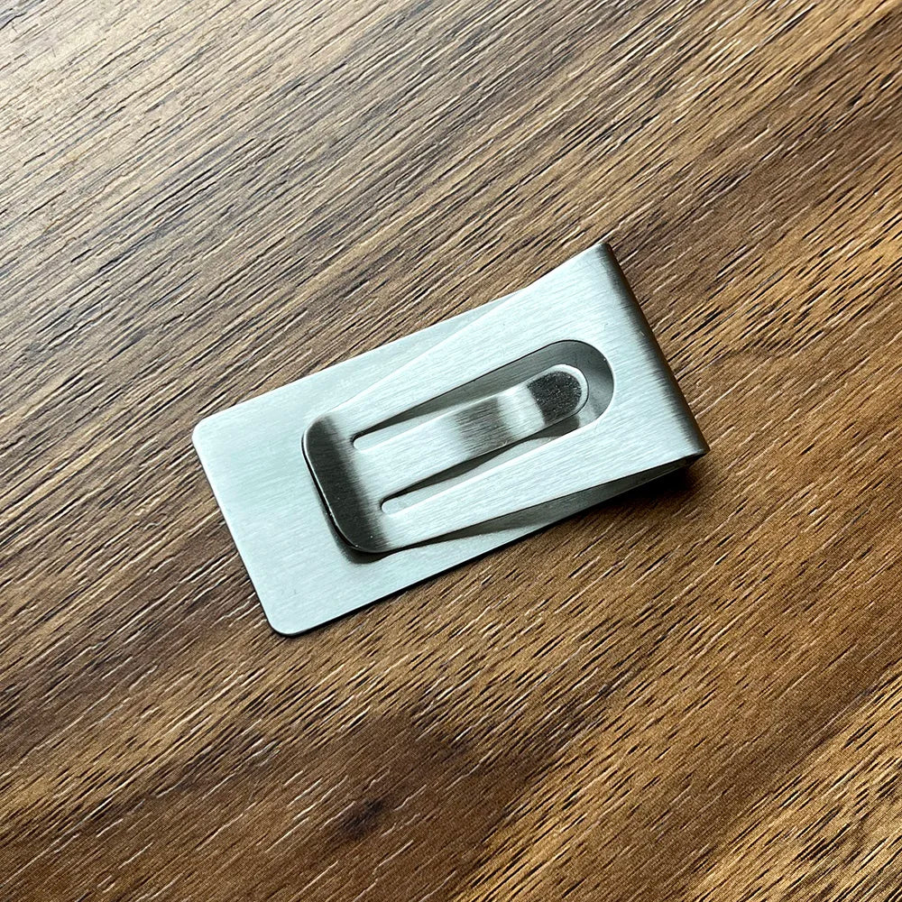 A silver personalized engraved money clip wallet lying on a dark wooden surface.