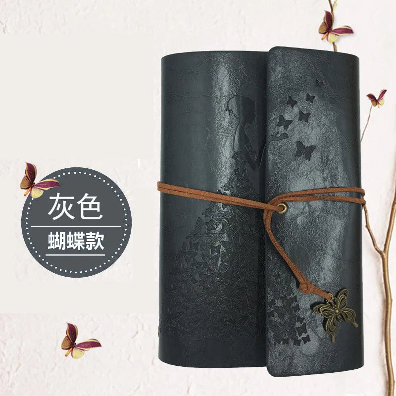 A dark gray cylindrical notebook with a leather texture and a brown cord tied around it, featuring butterfly designs.