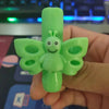 A hand holds a bright green silicone pencil grip shaped like a smiling bee for handwriting aid.