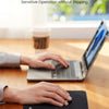 A hand is using a black non-slip rubber mouse pad on a wooden desk in front of an open laptop.
