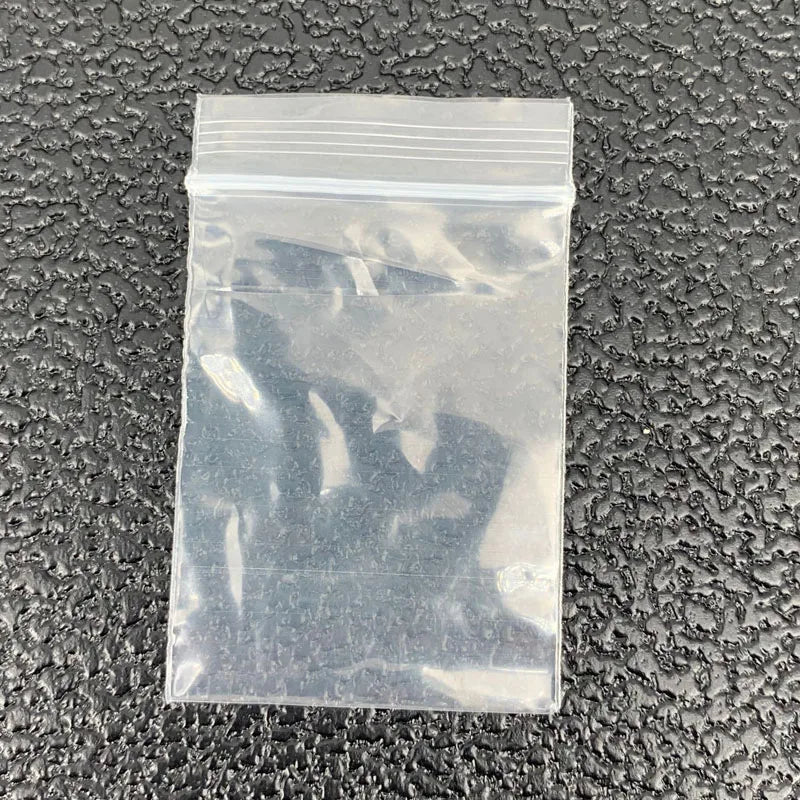 A clear plastic ziplock jewelry bag lying on a dark textured surface.