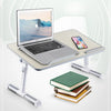 A silver laptop is placed on a portable adjustable desk stand next to a smartphone and a stack of books.