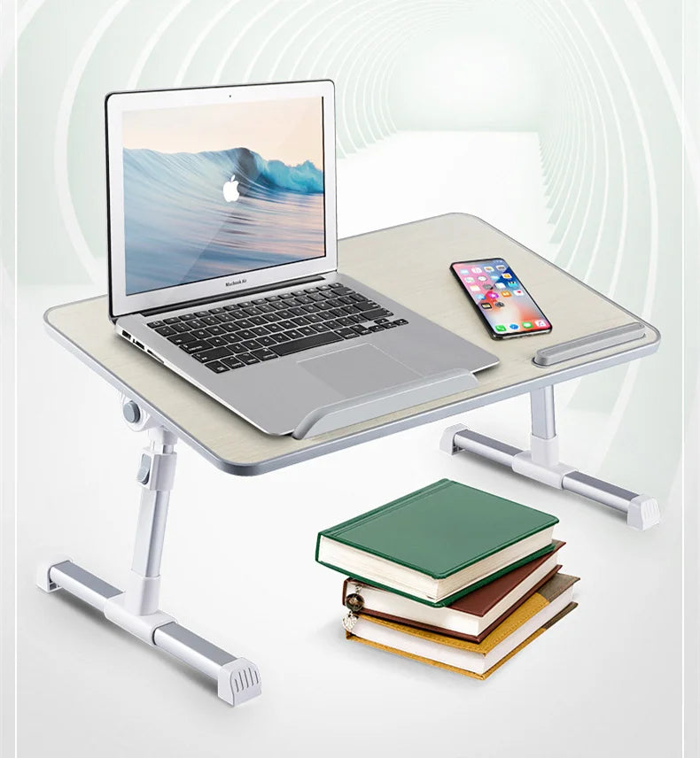 A silver laptop is placed on a portable adjustable desk stand next to a smartphone and a stack of books.