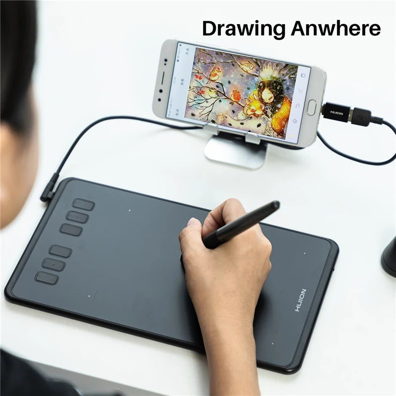 Une main dessine sur une tablette numérique noire, tandis qu'un smartphone affiche une application de dessin.