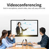 A woman is shown on a large monitor during a video conference call with several people in a meeting room.