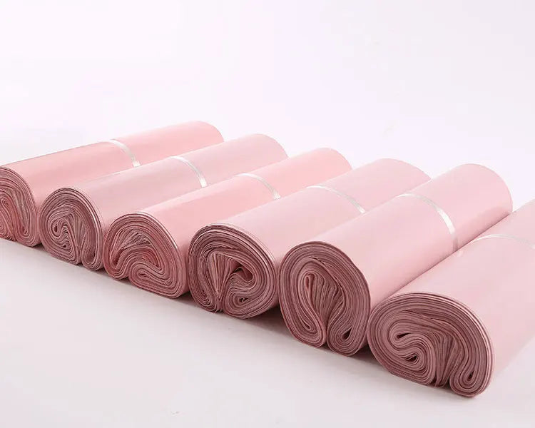Rolls of pink waterproof self-seal poly mail bags arranged in a line.