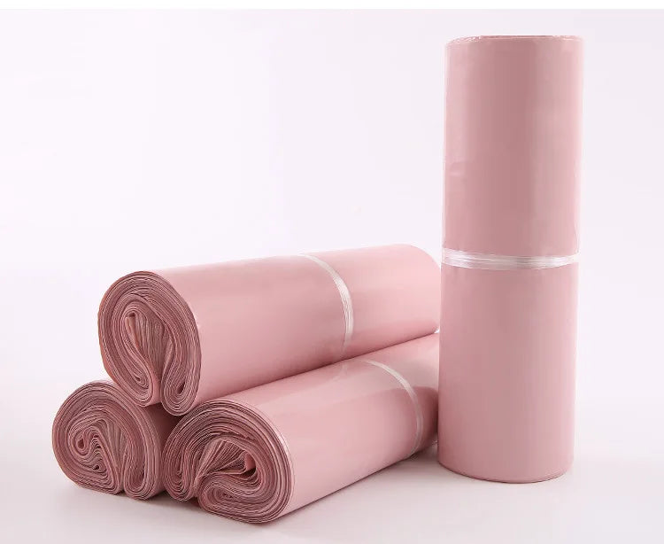 Rolls of pink waterproof self-seal poly mail bags stacked and standing upright.