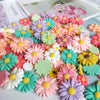 A colorful assortment of pink, purple, yellow, and green sunflower flatback resin cabochons for crafts.