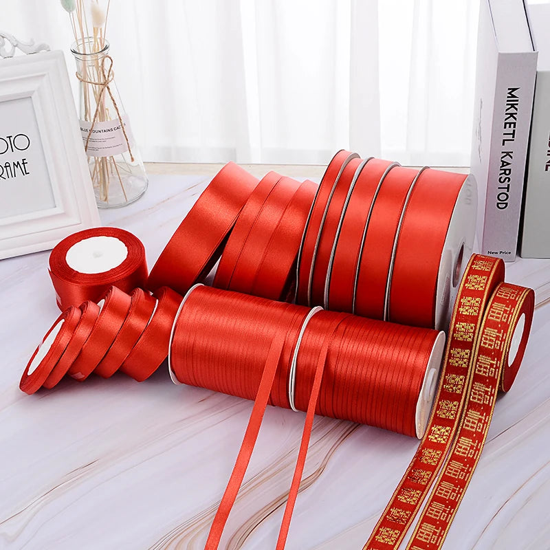 A collection of red satin ribbon spools and rolls for crafts and decor displayed on a white surface.