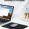 A black non-slip rubber mouse pad with a gray mouse is placed on a white desk next to a laptop.