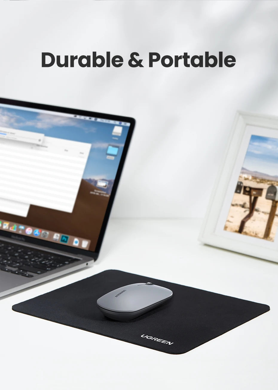 A black non-slip rubber mouse pad with a gray mouse is placed on a white desk next to a laptop.