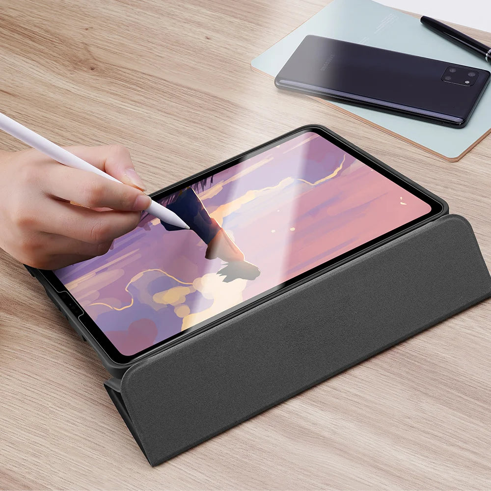 A hand writes on a paper-feel matte screen protector for an iPad placed on a wooden table.
