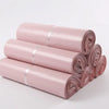 Rolls of pink waterproof self-seal poly mail bags stacked diagonally on a white surface.