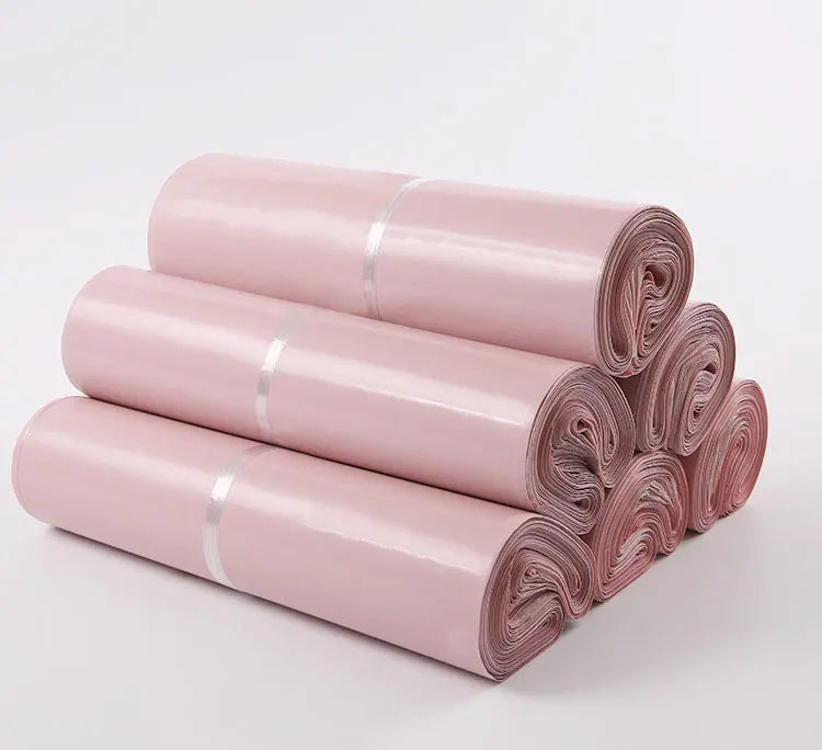Rolls of pink waterproof self-seal poly mail bags stacked diagonally on a white surface.