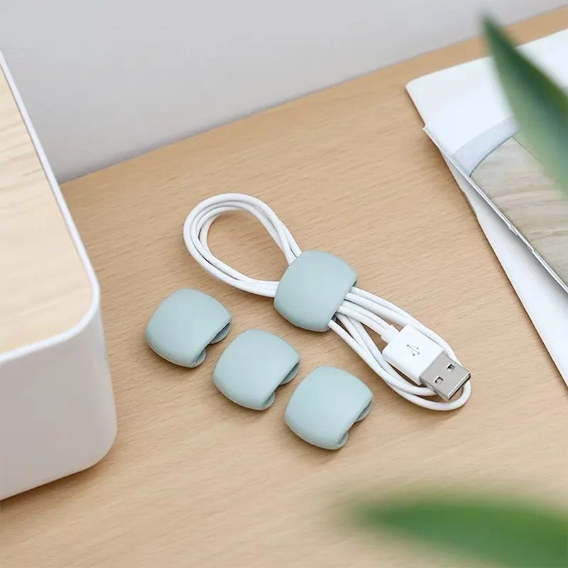 A set of light green silicone cable organizer clips and a white USB cable lying on a wooden surface.
