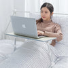 A woman is using a portable adjustable laptop desk stand to position a silver laptop on her lap while sitting on a bed.