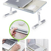 A portable adjustable laptop desk stand with a light gray finish, shown in use on a table.