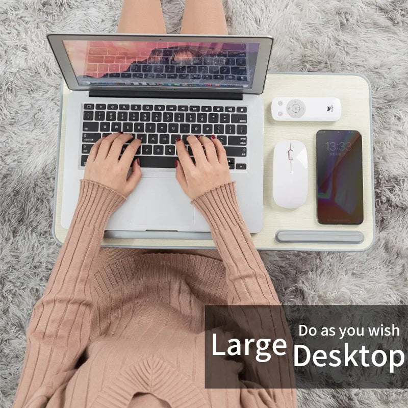 A person wearing a beige sweater is using a portable laptop desk stand with a laptop, mouse, and smartphone.
