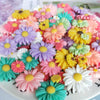 A colorful arrangement of pink, yellow, purple, and green flower-shaped resin cabochons for crafts.