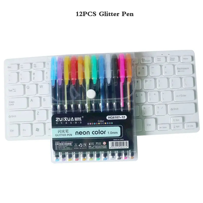 A set of 12 glitter pens in various colors displayed next to a laptop keyboard.