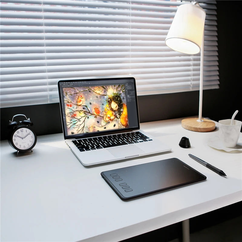 Une tablette graphique numérique de précision est placée sur un bureau blanc à côté d'un ordinateur portable et d'une lampe.