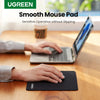 A hand is placing a black non-slip rubber mouse pad on a wooden desk in front of a laptop.