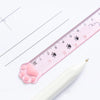 A pink plastic ruler marked with cat paw prints is shown next to a white pen on a white background.