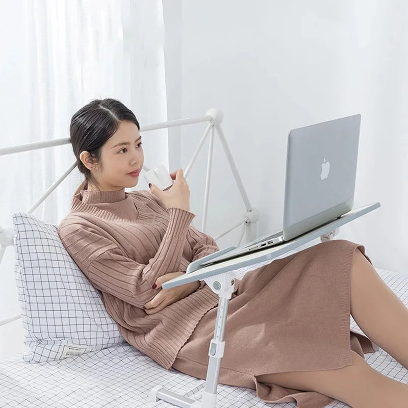 A woman is using a portable adjustable laptop desk stand to position a silver laptop on her lap.