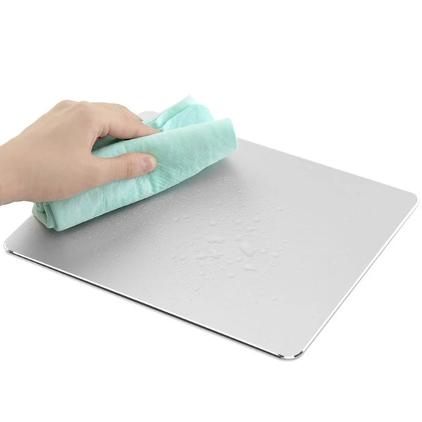 A hand is wiping a white mouse pad with a light green cloth.