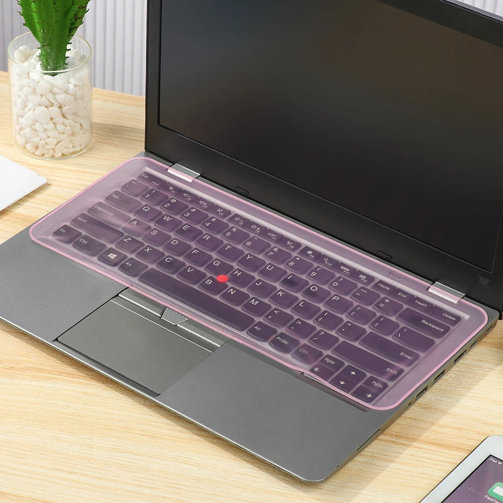 Laptop-Tastatur mit pinker Silikonfolie, auf einer Holzoberfläche gelegen.