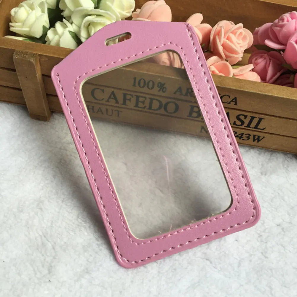 A pink PU leather ID card holder with a clear window is displayed on a wooden tray surrounded by pink and peach roses.