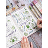 A hand holds an open notebook filled with watercolor illustrations and a set of three retro twin markers.