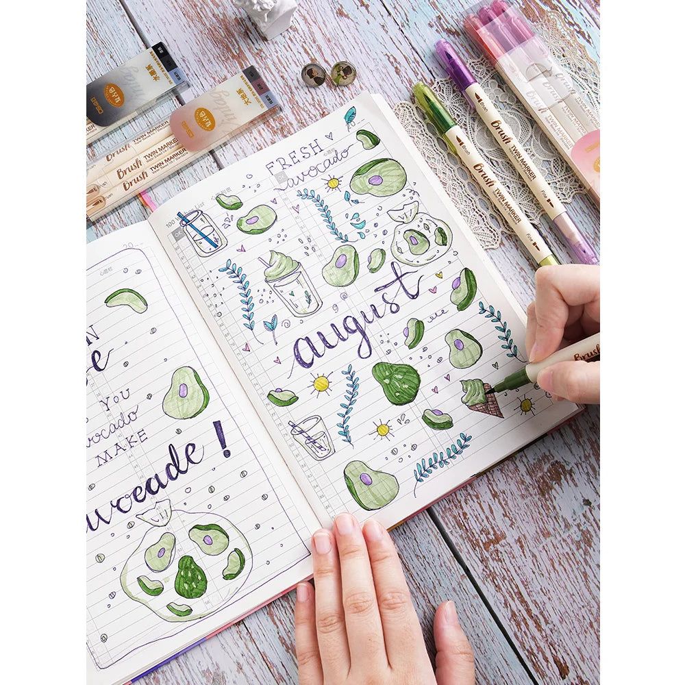 A hand holds an open notebook filled with watercolor illustrations and a set of three retro twin markers.
