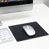 A black mouse pad with a silver wireless mouse is placed on a white surface.