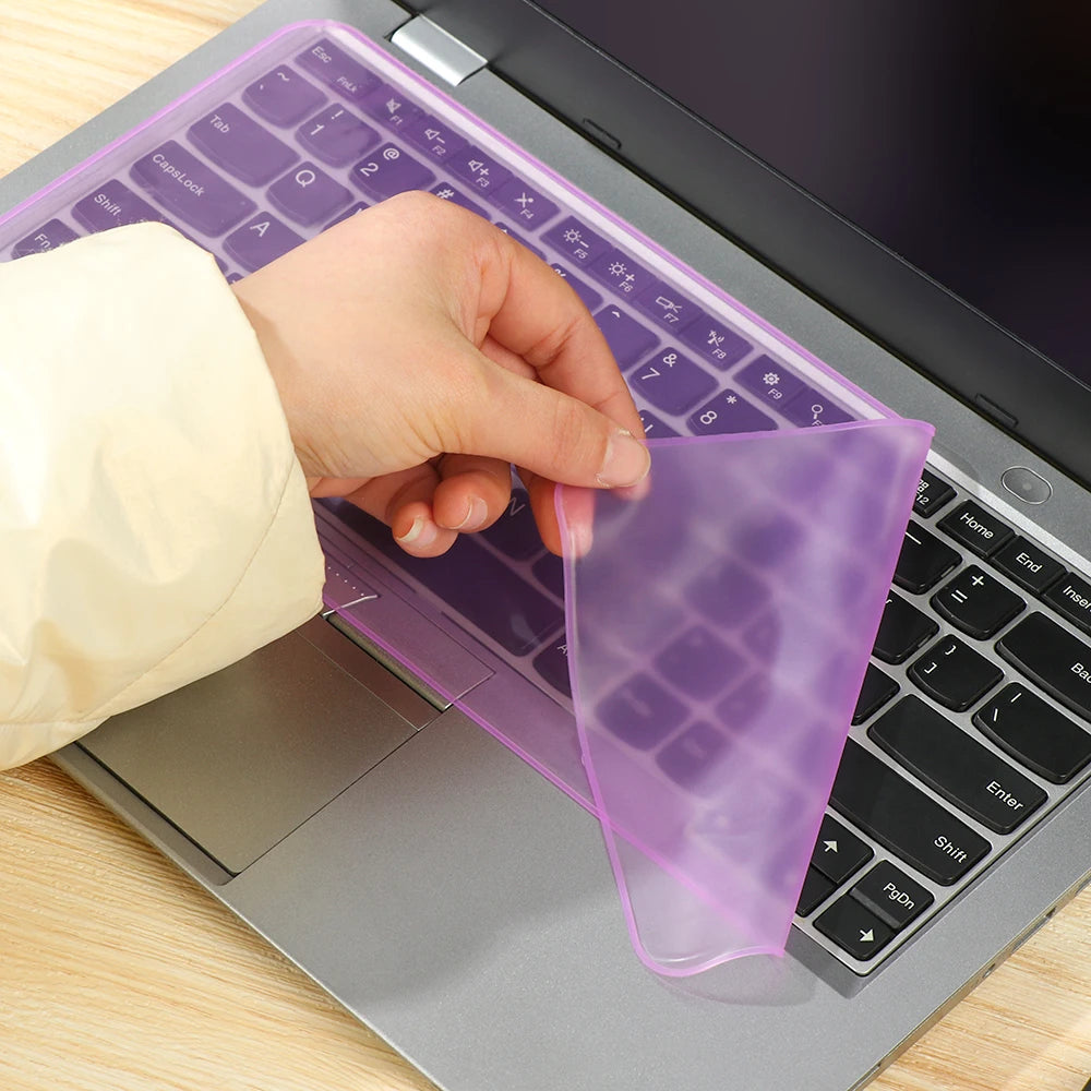 Eine Hand legt eine lila Silikon-Keyboard-Schutzfolie auf eine Laptop-Tastatur.