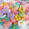 A colorful arrangement of pink, yellow, purple, and green sunflower flatback resin cabochons for crafts.