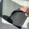 A hand is opening a dark gray composition book cover to reveal a perforated metal grid inside.