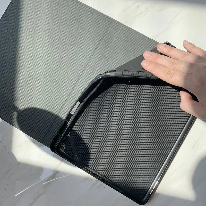 A hand is opening a dark gray composition book cover to reveal a perforated metal grid inside.