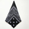 Black bandana square scarf with white paisley print folded into a triangle shape