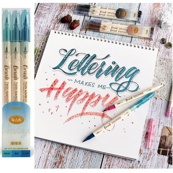 A set of three brush twin markers in various shades and colors is displayed next to a notebook with lettering practice.