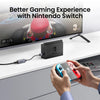 A hand holds a Nintendo Switch console and an adapter plugged into a computer setup for gaming.